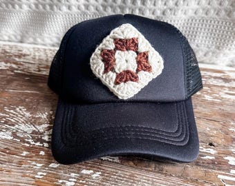 May include: A black trucker hat with a brown and white crocheted square patch on the front.