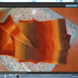 Peut inclure: Un gilet sans manches en tricot avec un d&eacute;grad&eacute; de couleurs orange, marron et jaune. Le gilet est pli&eacute; en deux et pos&eacute; &agrave; plat sur une table.