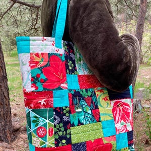 Puede incluir: Una bolsa de mano acolchada con un diseño de patchwork que presenta telas rojas, verdes y azules. La bolsa tiene correas turquesa y está hecha de una variedad de patrones diferentes.
