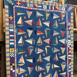 Może przedstawiać: Niebieska kołdra w stylu marynistycznym z wzorem żaglówek wykonanych z kolorowych skrawków tkaniny. Kołdra jest obszyta różnymi kolorowymi tkaninami, w tym czerwoną, białą i niebieską.