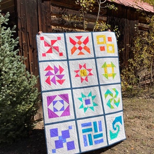 May include: A colorful quilt with a variety of geometric patterns in shades of blue, green, purple, orange, and yellow. The quilt is made up of 12 squares, each with a different design.