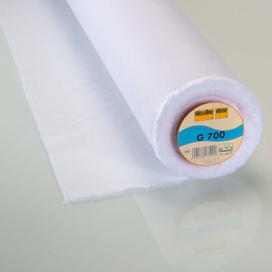 May include: A white roll of Vlieseline Vilene G 700 interfacing fabric. The label is yellow with blue text and a blue and white icon. The label reads "Vlieseline Vilene G 700 90 cm x 25 m 100% CO."