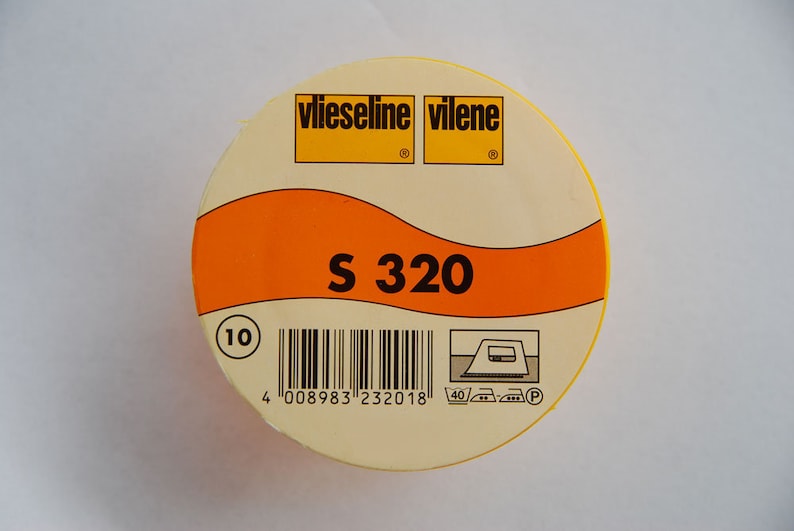 May include: A yellow and orange round container with the text "Vlieseline Vilene" and "S 320" printed on it. The container has a barcode and a washing instruction symbol.
