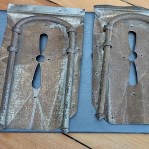 Puede incluir: Dos paneles de metal oxidado con un recorte decorativo en forma de hélice. Los paneles tienen un aspecto desgastado y envejecido y están unidos a una superficie gris.