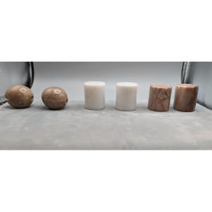 May include: Six stone beads and cylinders are displayed. Two oval beads with a brown, speckled appearance are on the left. Two white, cylindrical beads are in the centre, and two brown, textured cylinders are on the right.