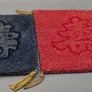 May include: Two square fabric pouches with a textured finish. One is navy blue, the other red. Each has a large, embroidered Chinese double happiness symbol in a contrasting colour. Gold tassels decorate the corners.