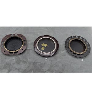 May include: Three decorative trays with dark interiors and ornate, openwork rims. The trays are in shades of brown and black, with gold and silver accents. The trays are circular and appear to be made of metal.
