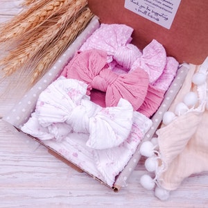 May include: A gift box filled with three pink and white fabric headbands with bows. The headbands are in a white box with pink polka dots. The box is sitting on a light wood surface. "Thank you for supporting a small business" is written on the box.