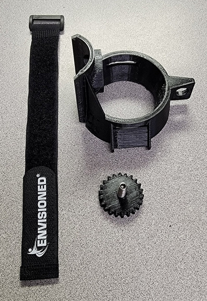 May include: A black 3D printed camera mount with a black velcro strap and a black gear with a silver screw. The strap has the text "ENVISIONED" printed on it.