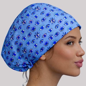 May include: A light blue surgical scrub cap with a repeating pattern of stylized blue eyes. The cap is tied in the back and worn by a person in a navy blue scrub top.