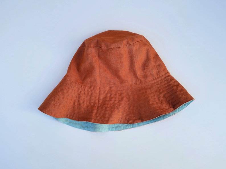 Op de afbeelding: Een bruine linnen bucket hat met een blauwe voering. De hoed heeft een brede rand en een eenvoudig ontwerp.