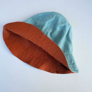 Puede incluir: Un sombrero de cubo reversible con un exterior azul turquesa y un interior naranja &oacute;xido.