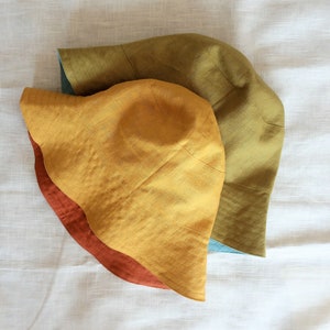 Puede incluir: Tres sombreros de sol de diferentes colores: un sombrero amarillo mostaza, un sombrero verde y un sombrero azul. Los sombreros est&aacute;n hechos de una tela suave y texturizada.