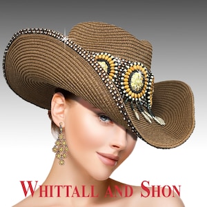 May include: A brown cowboy hat with a wide brim, decorated with beads and a central embellishment. The hat has a detailed design with a mix of colours and textures, and the text "Whittall and Shon" is visible at the bottom.