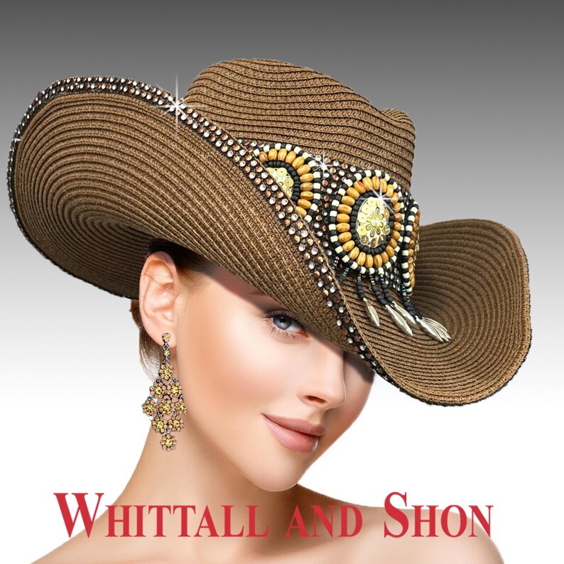 May include: A brown cowboy hat with a wide brim, decorated with beads and a central embellishment. The hat has a detailed design with a mix of colours and textures, and the text "Whittall and Shon" is visible at the bottom.