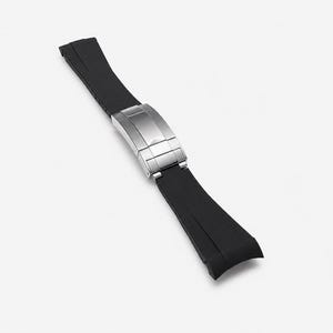 May include: A black rubber watch strap featuring a brushed stainless steel deployment clasp. The strap consists of two segments connected by the central metal buckle mechanism, designed with a smooth finish and curved ends for attachment to a watch case.