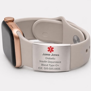 Puede incluir: Un reloj inteligente con una correa beige y una caja de oro rosa. Una placa metálica en la correa muestra información médica, incluido un símbolo médico rojo, el nombre "Jaime Jones" y detalles médicos para la diabetes.