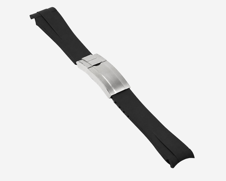 Puede incluir: Una correa de reloj de goma negra con un cierre de acero inoxidable. La correa est&aacute; en &aacute;ngulo diagonalmente sobre un fondo blanco. El cierre es de color plata cepillada.