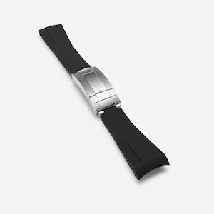 May include: A black rubber watch strap featuring a brushed silver-tone metal deployment clasp. The strap consists of two segments connected by the central folding buckle mechanism, designed with a smooth finish and curved ends for watch attachment.