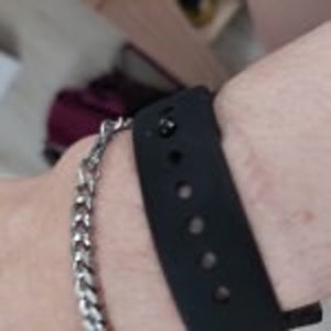Close up view of the pin closure on a black silicone bracelet band being worn on an adult's wrist.