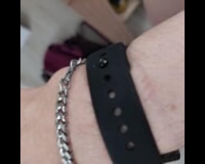 Close up view of the pin closure on a black silicone bracelet band being worn on an adult's wrist.