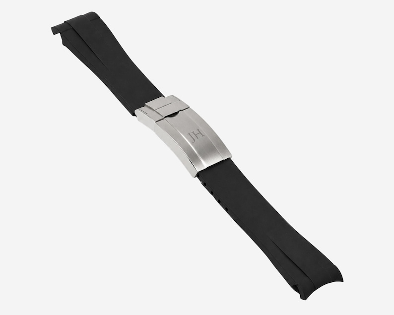 Puede incluir: Una correa de reloj de goma negra con un cierre plateado. El cierre tiene las iniciales "JH" grabadas. La correa est&aacute; dise&ntilde;ada para ser duradera y c&oacute;moda para el uso diario.