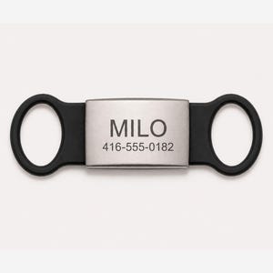 May include: A black and silver pet ID tag with the name "MILO" and a phone number. The tag has two circular loops on either end and a rectangular centre.