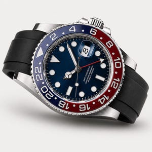 Puede incluir: Un reloj de pulsera de acero inoxidable con esfera azul, bisel rojo y azul y correa de caucho negro. El reloj presenta marcadores de hora y agujas blancas, con visualizaci&oacute;n de fecha a las 3. Modelo GMT-Master II.