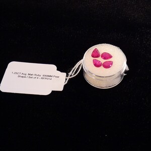 May include: A set of four pink pear-shaped rubies in a clear plastic container. The label reads "1.25CT Avg. Mah Ruby 8X6MM Pear Shape / Set of 4 - RFP014".