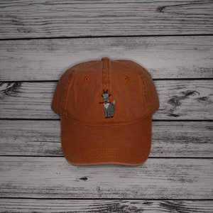 Puede incluir: Una gorra de béisbol marrón con una imagen bordada de una cabra comiendo una zanahoria.