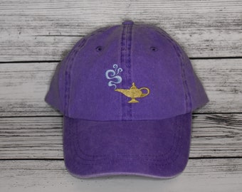 May include: A purple baseball cap with an embroidered image of a golden lamp with blue smoke coming out of it.