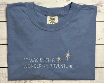 Puede incluir: Una camiseta azul claro con el texto "It was such a wonderful adventure" bordado en blanco con dos estrellas blancas.