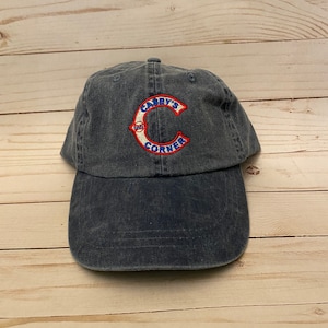 May include: A dark blue denim baseball cap with a red, white, and blue embroidered patch that says "Casey's Corner" with a large "C" in the center.