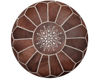 May include: A brown leather pouf with a white embroidered star design. The pouf is made of many stitched leather panels.