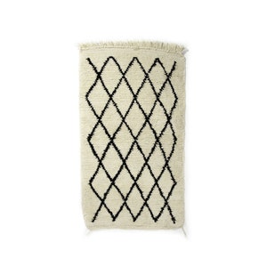 May include: A white rug with a black diamond pattern. The rug has a fringed border.