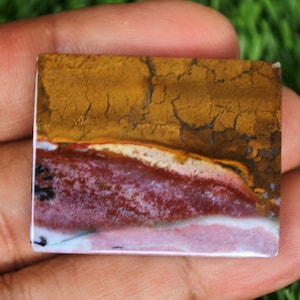 May include: A rectangular, polished, multi-colored agate cabochon with a brown, yellow, white, and pink color pattern. The cabochon has a smooth, polished surface and a natural, organic shape.