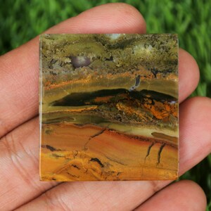 May include: A square-shaped, polished, multi-coloured agate stone with brown, yellow, green, and black banding. The stone has a natural, organic pattern.