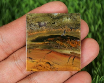 May include: A square-shaped, polished, multi-coloured agate stone with brown, yellow, green, and black banding. The stone has a natural, organic pattern.