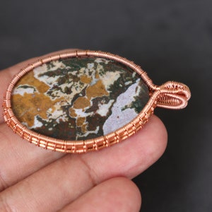 May include: A copper wire wrapped pendant featuring a colourful agate stone with brown, white and green patterns.