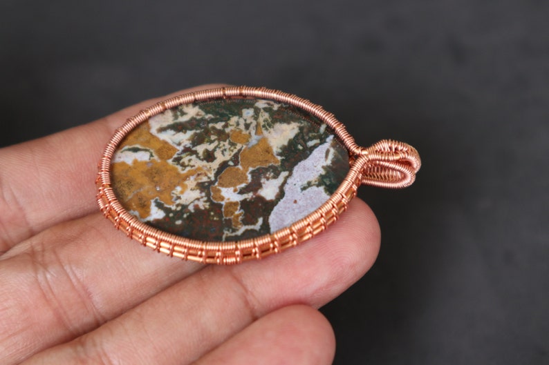 May include: A copper wire wrapped pendant featuring a colourful agate stone with brown, white and green patterns.