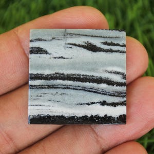 May include: A square, black and white banded agate cabochon with a polished surface. The stone has a natural, organic pattern of black and white stripes.