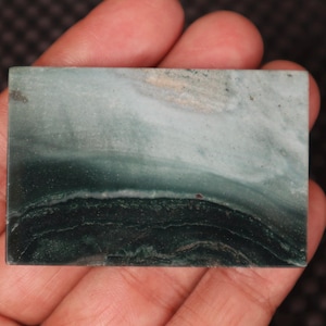 May include: A green and white agate cabochon with a layered pattern. The cabochon is smooth and polished.