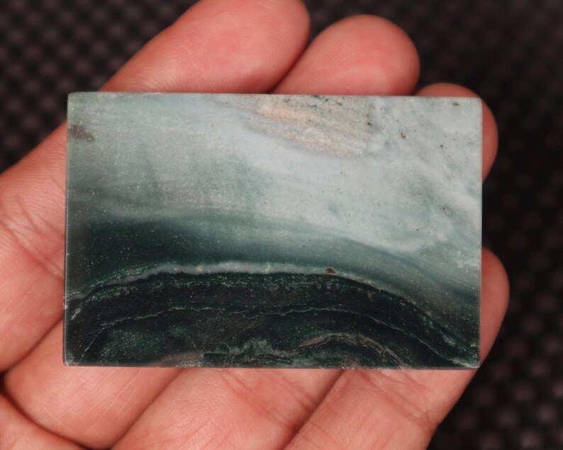 May include: A green and white agate cabochon with a layered pattern. The cabochon is smooth and polished.