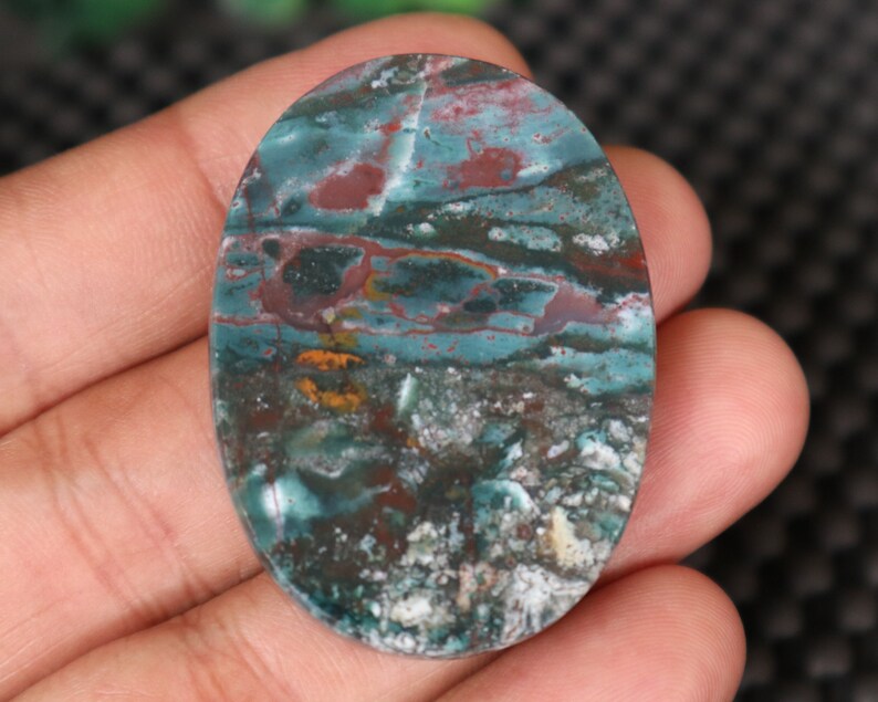 Pode incluir: Caboch&atilde;o oval de &aacute;gata verde, marrom e branco com um padr&atilde;o de redemoinho.