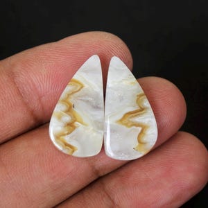 May include: Pair of white agate cabochons with brown and white patterns. The cabochons are teardrop shaped and have a smooth, polished finish.