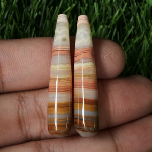 May include: Pair of long, pointed, multi-coloured agate cabochons with a banded pattern in shades of brown, orange, pink, and white.