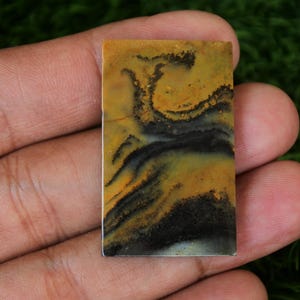 May include: A rectangular, yellow, black, and white agate cabochon with a swirling pattern. The cabochon is about 2 inches long and 1 inch wide.
