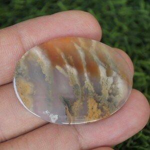Puede incluir: Un cabujón de ágata redondo y pulido con una mezcla de colores marrón, blanco y gris. La piedra tiene un patrón único y arremolinado.
