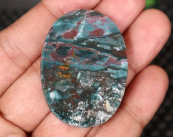 May include: An oval cabochon gemstone with a swirling pattern in shades of green, brown, and white. The stone is polished and has a smooth surface.