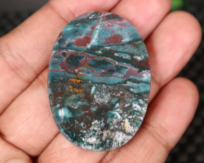 Pode incluir: Uma pedra preciosa oval em caboch&atilde;o com um padr&atilde;o de redemoinho em tons de verde, marrom e branco. A pedra &eacute; polida e tem uma superf&iacute;cie lisa.